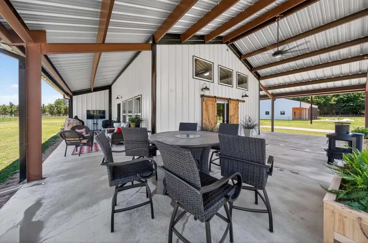Covered porch outdoor dining area with bar height seating and natural barn door entry, barndominium Chandler TX