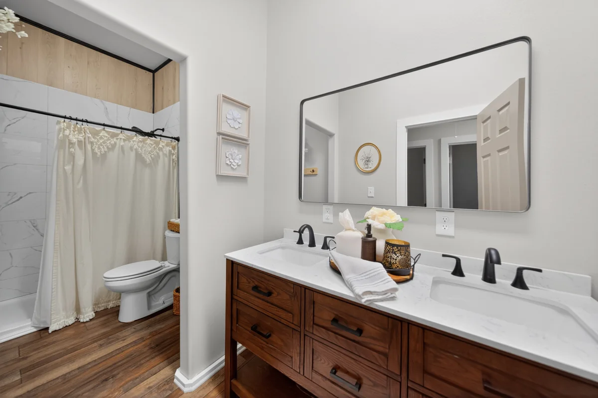 Guest bathroom with dark wood double vanity, quartz countertop, large mirror and matte black fixtures, barndominium Chandler TX