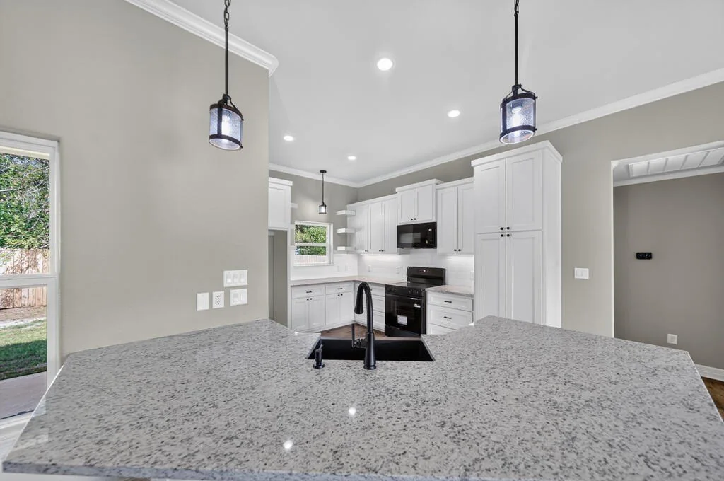 Kitchen seen across the granite peninsula and sink, with white cabinets and black appliances, at 281 ACR 308.