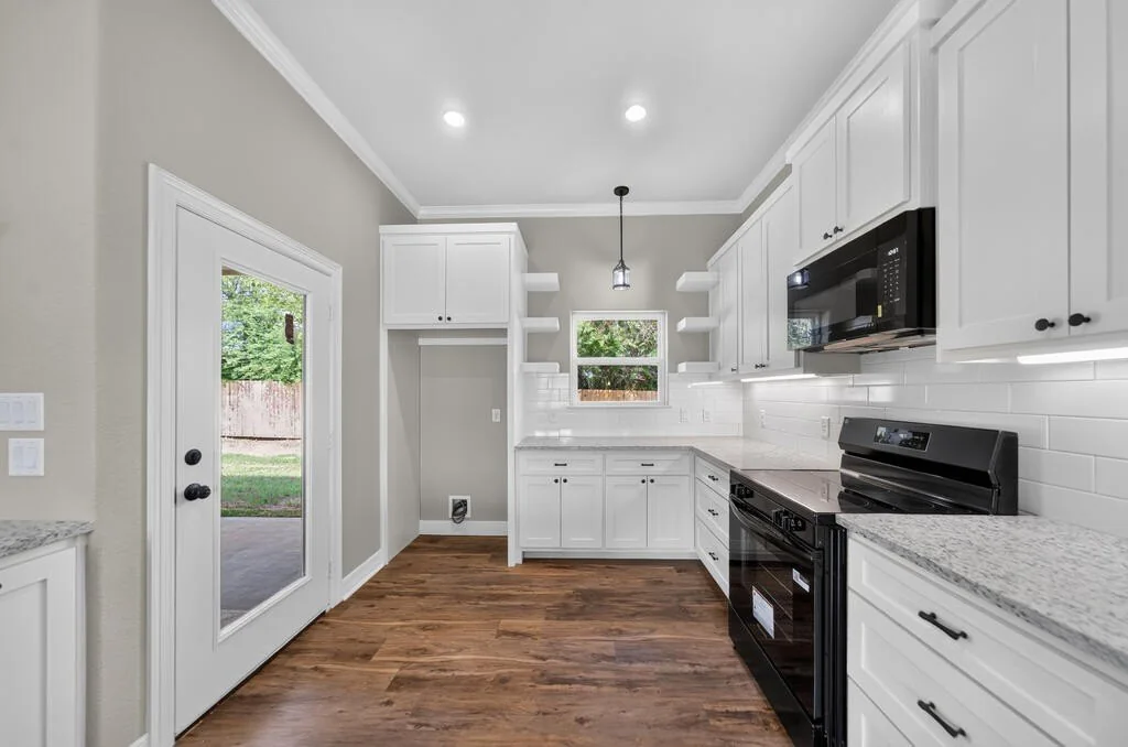 Kitchen range wall with subway tile, floating shelves and a black electric range and microwave at 281 ACR 308.