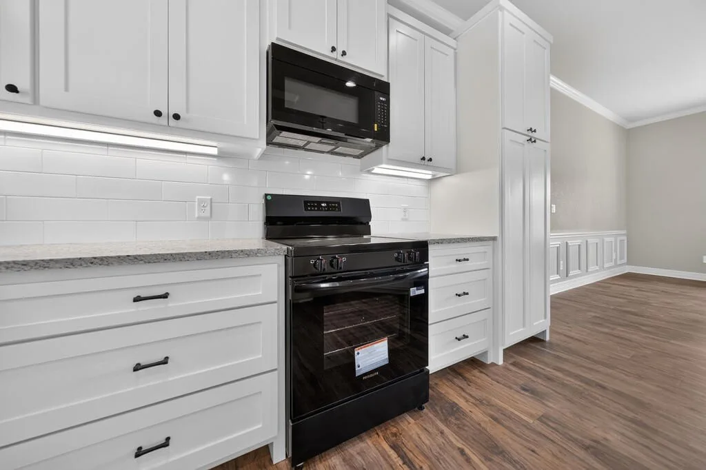 White kitchen cabinets with black hardware beside the electric range and a tall pantry cabinet at 281 ACR 308.