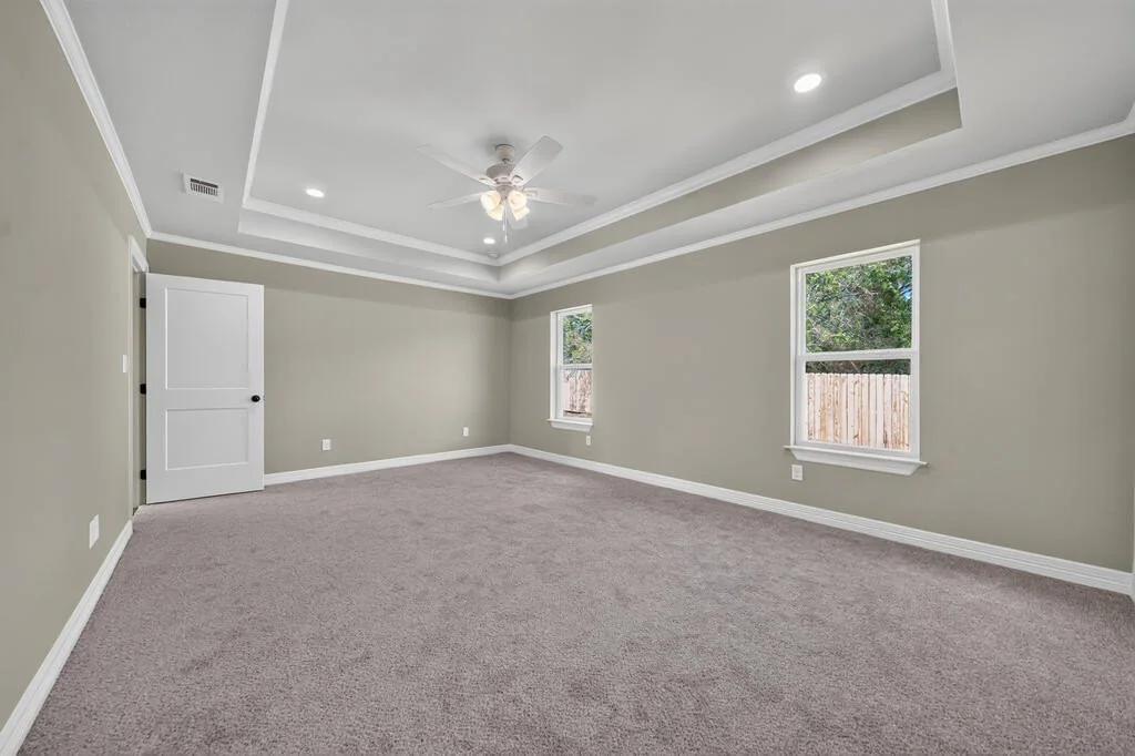 Primary bedroom with a tray ceiling, ceiling fan and two windows at 281 ACR 308.