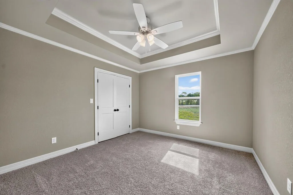 Carpeted bedroom with a tray ceiling, double closet doors and a window facing open land at 281 ACR 308.