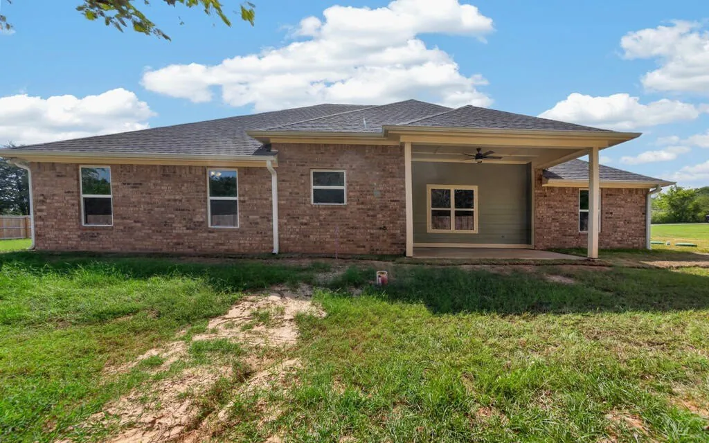 Back of the house with brick, a covered porch and the open backyard at 281 ACR 308.
