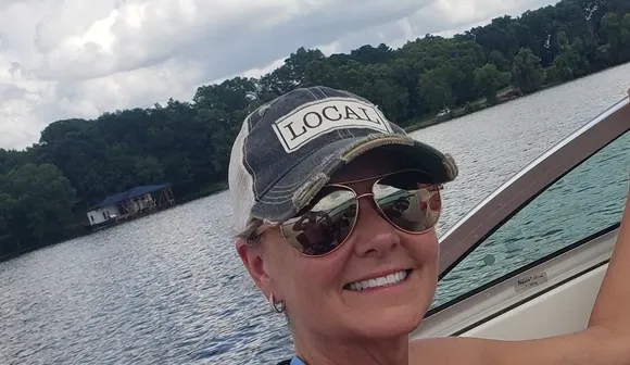 Charlene Hall, East Texas REALTOR&reg;, smiling in a LOCAL cap and sunglasses on a boat on Lake Palestine.