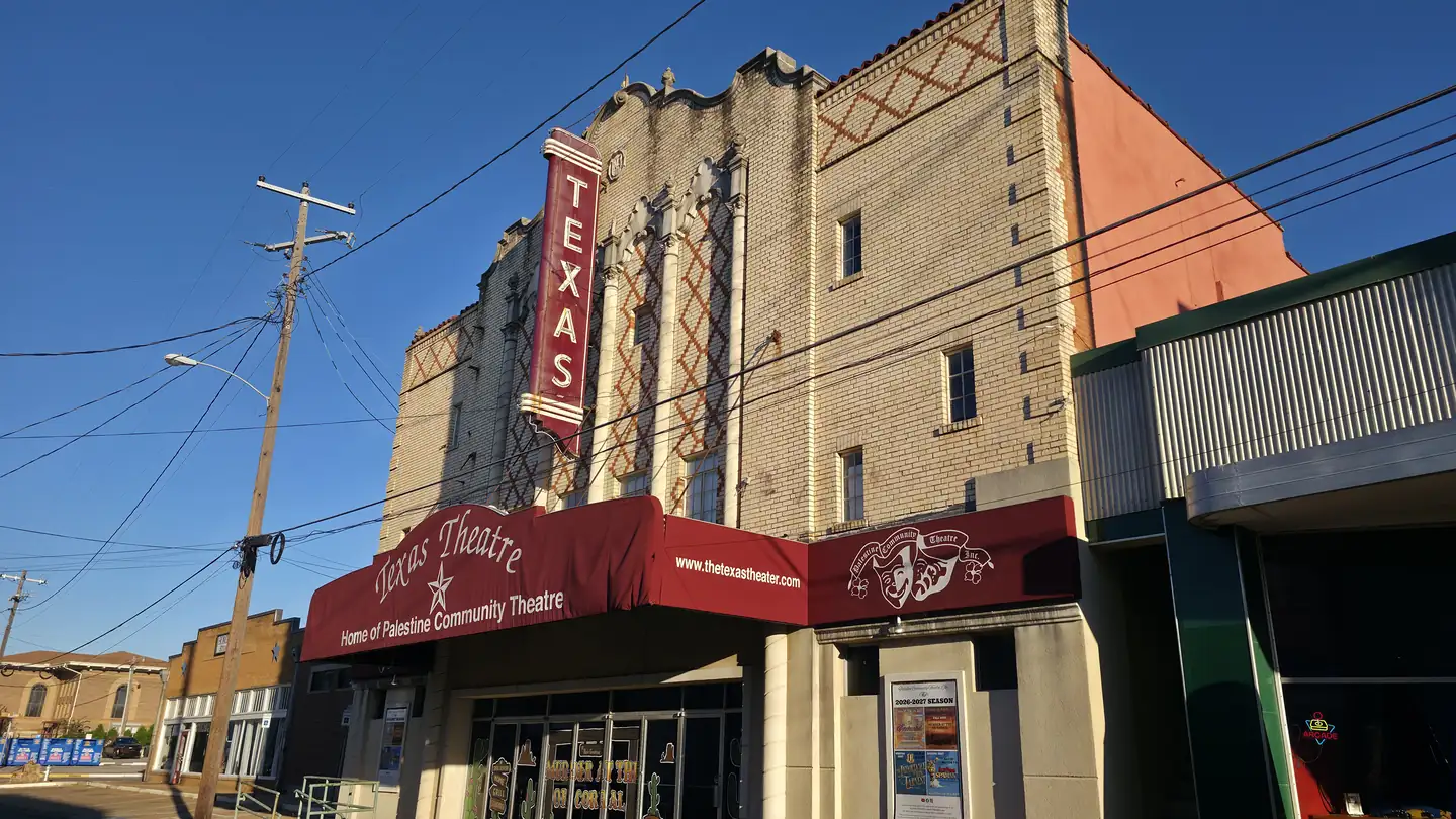 The Texas Theatre in downtown Palestine, Texas, with a tall red Texas sign, patterned brickwork and a red awning.