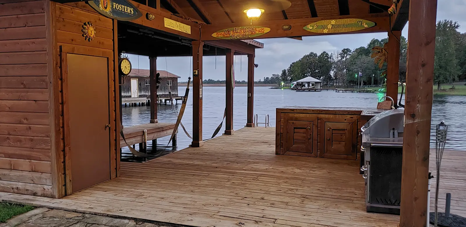 Inside a covered boathouse on Lake Palestine: a boat slip with lift straps, deck boards, lighting, an outdoor kitchen counter and a storage closet.