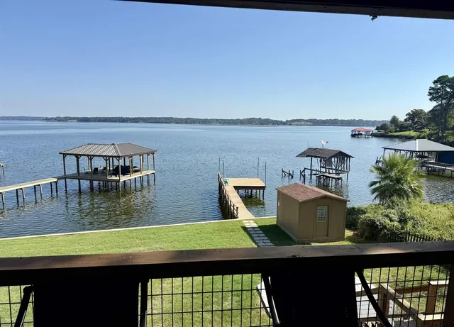 View of Lake Palestine from the back porch of 7359 E Panorama Dr in Brierwood Bay, looking down the lawn to the storage building and the pier with its open deck.