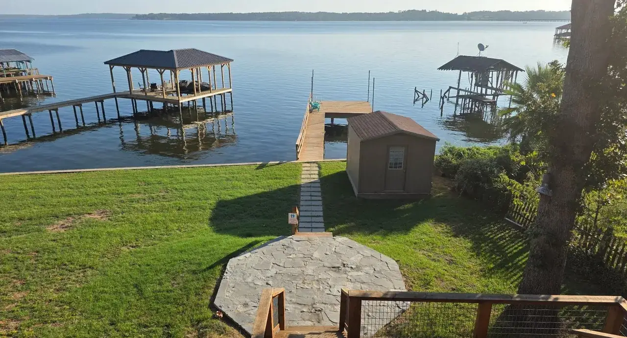 The pad between the cottage and the water at 7359 E Panorama Dr, with the walkway, storage building and pier beyond it on Lake Palestine.